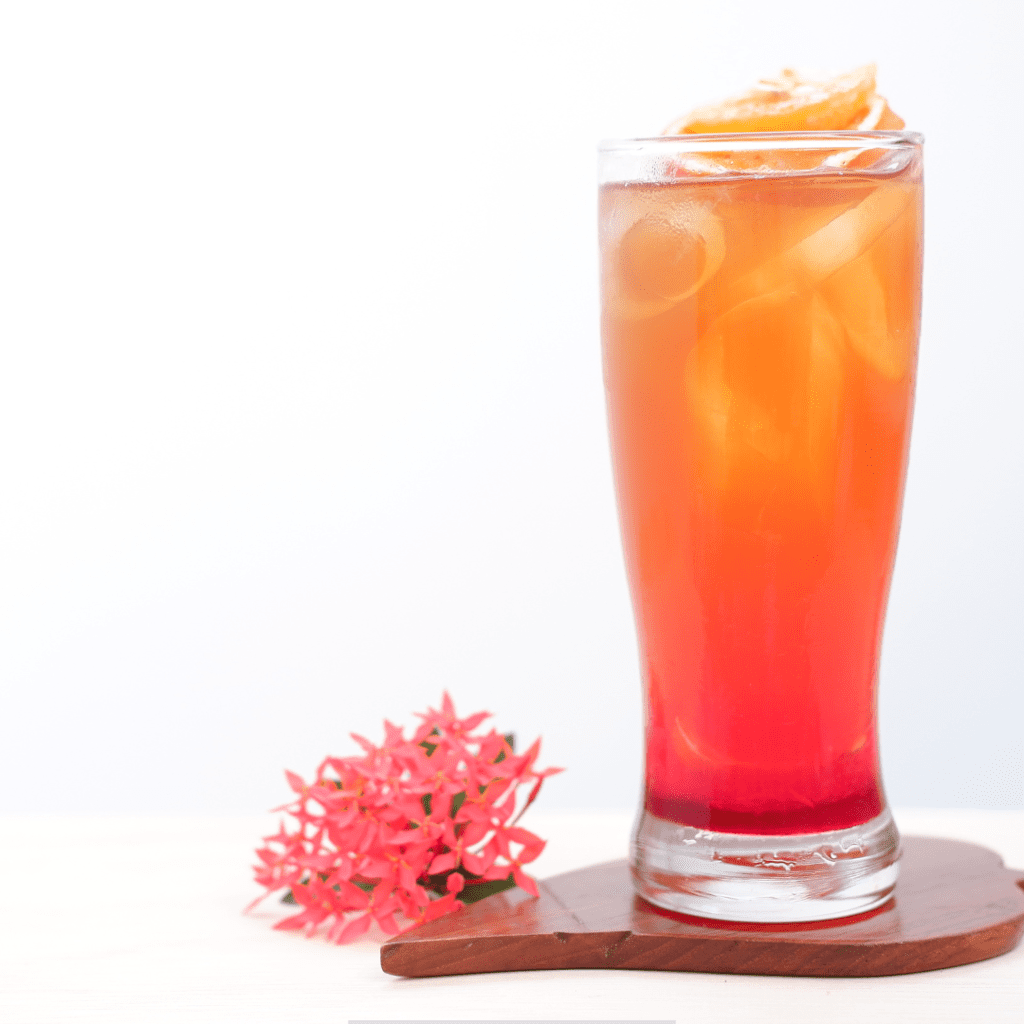 Calico Jack Rum Punch with a beautiful sunset color, topped with a twisted peel of orange, rested on a wooden tray with flowers beside